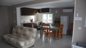 Un espacio habitable compacto con sofá, mesa de comedor, sillas, zona de cocina y un refrigerador.