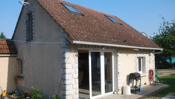 Una casa pequeña de un piso con techo inclinado, puerta corrediza de vidrio y un pequeño patio.