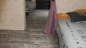 Un dormitorio con techo inclinado, cama de madera, dosel púrpura y una puerta visible que conduce a otra habitación.