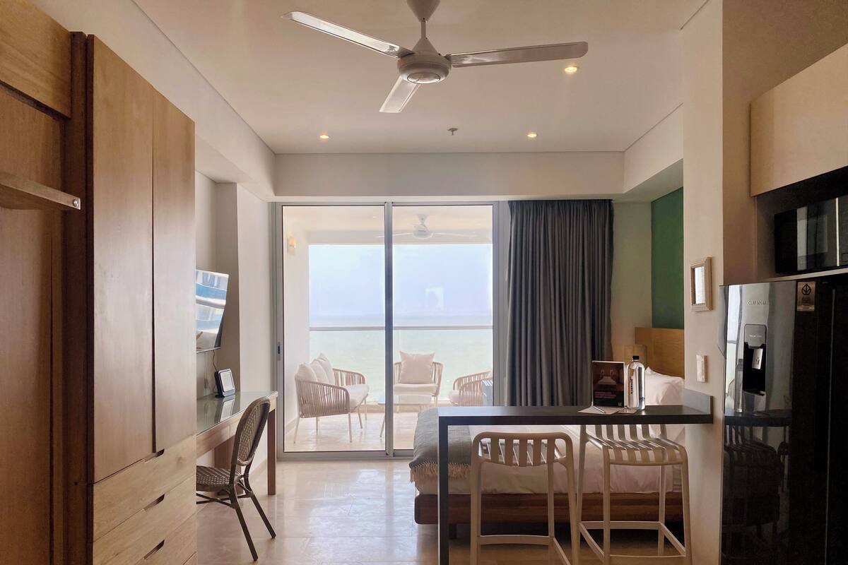 A modern hotel room with a balcony, a dining area, and a kitchenette.