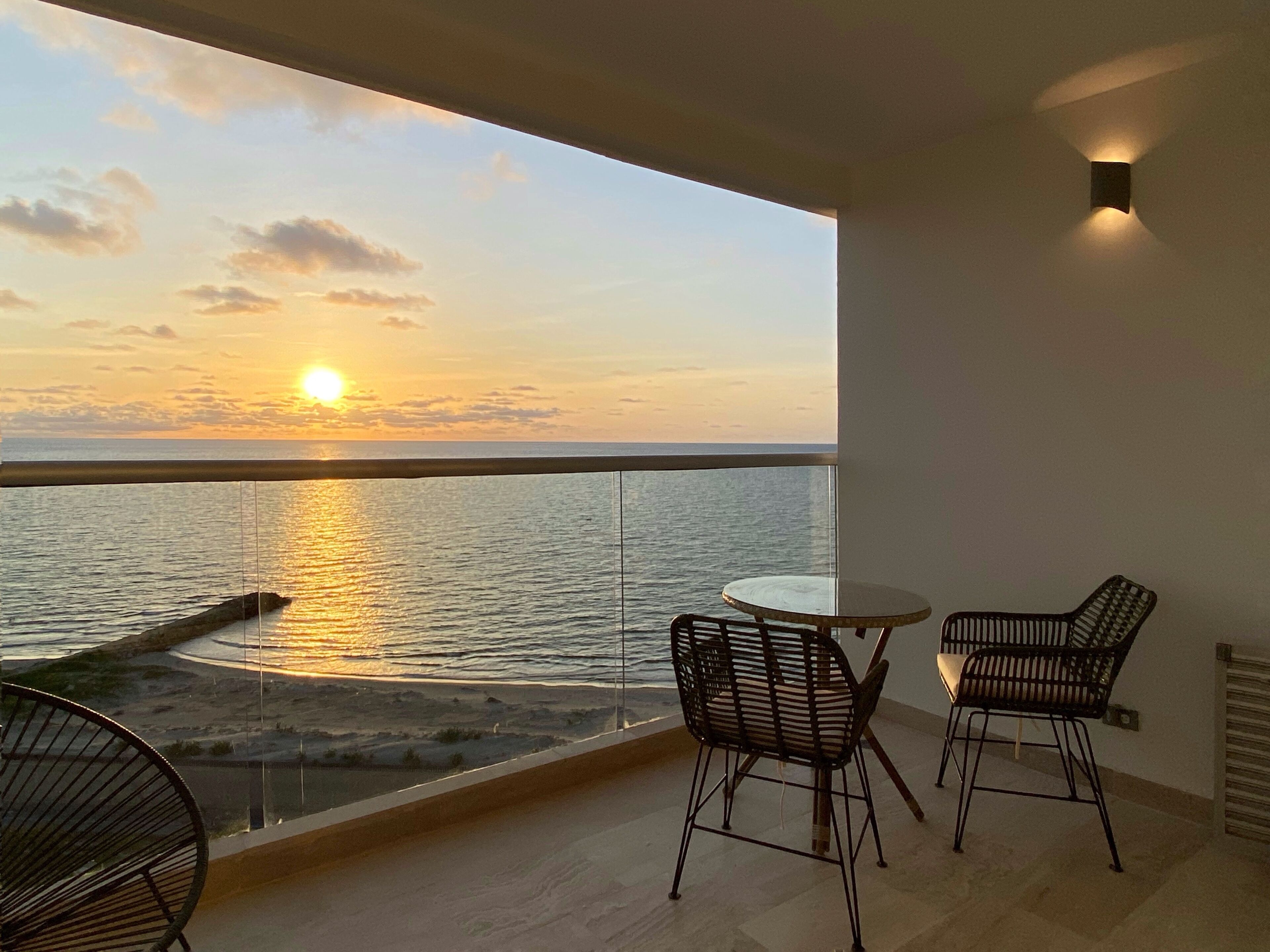 Ein Balkon mit Blick auf den Sonnenuntergang über dem Meer, zwei Stühle und ein kleiner Tisch.