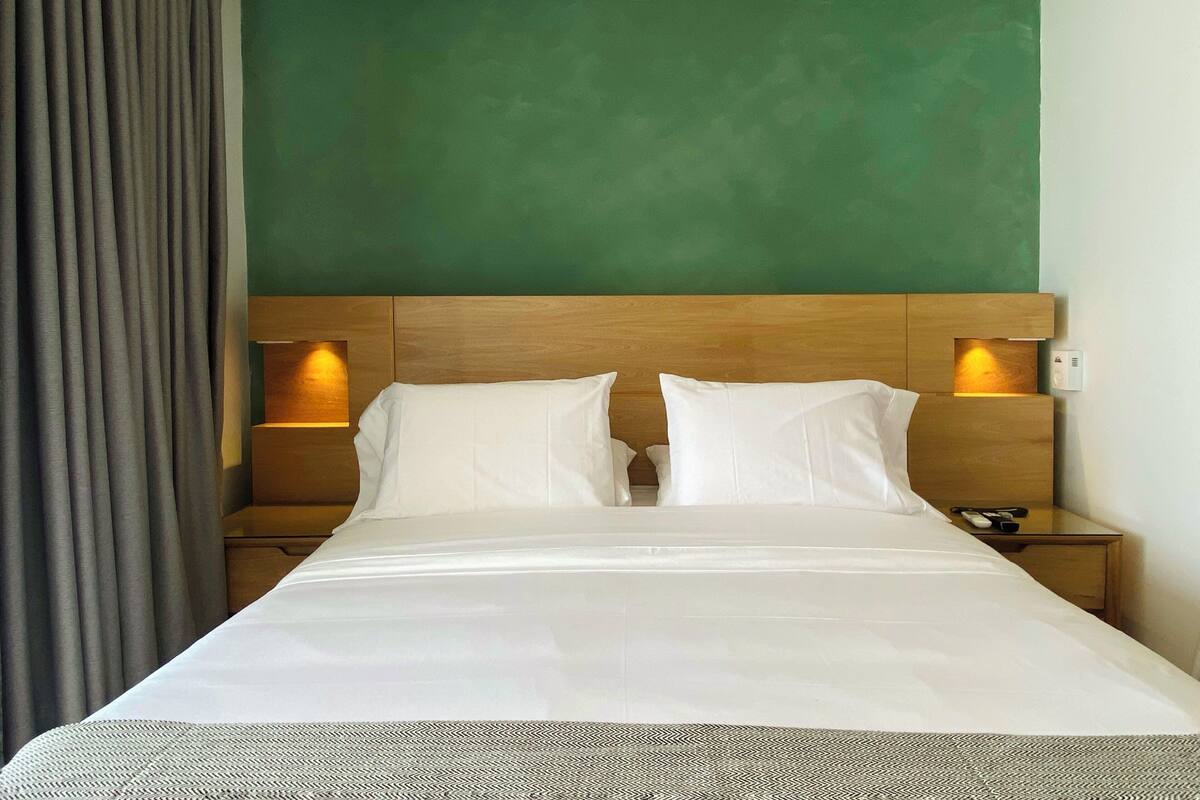 A hotel room with a large bed, wooden headboard, two bedside tables with lamps, and a green accent wall.