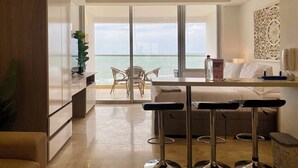 A modern hotel room with a balcony, a dining area, and a large window offering a view of the sea. - Wynwood Cartagena Beach (Cartagena)