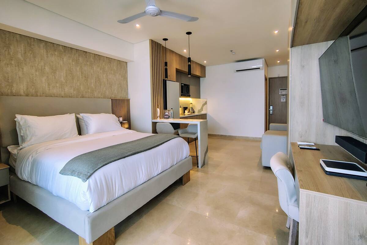 A modern hotel room with a large bed, a desk, a chair, a ceiling fan, and a flat-screen TV.