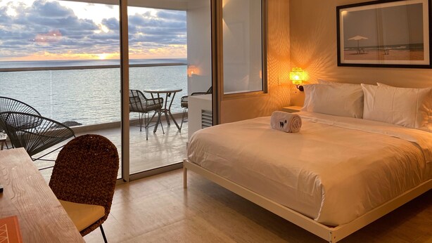 A bedroom with a bed, a desk, and a chair, a balcony with a table and chairs, and a view of the sea. - Wynwood Cartagena Beach (Cartagena)