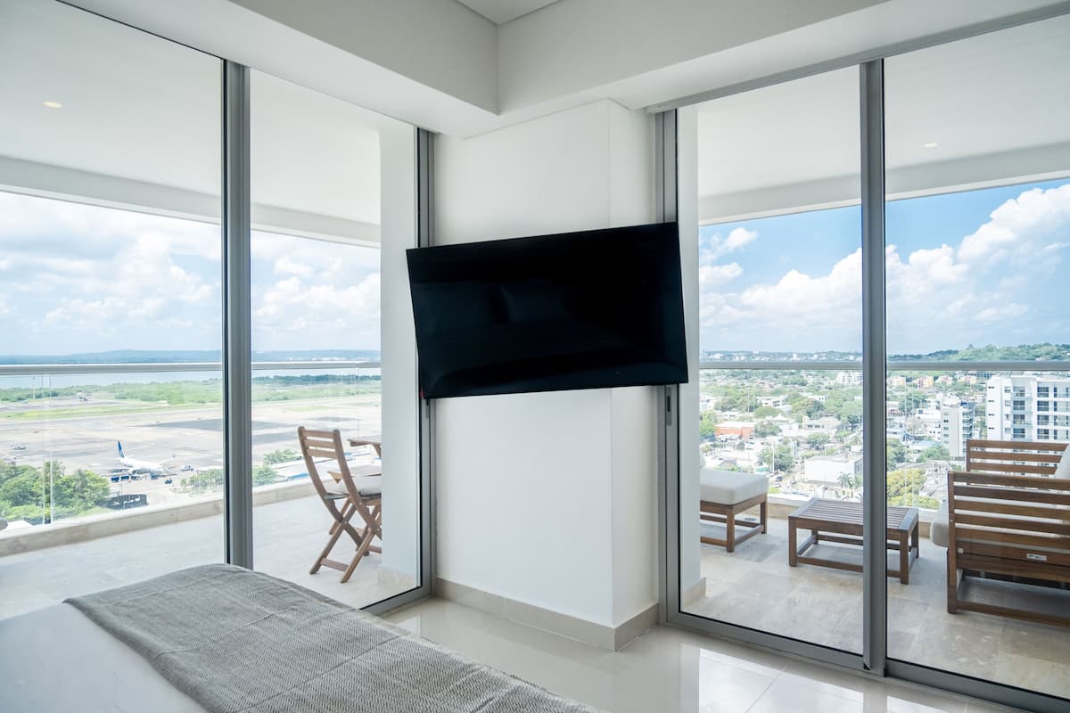 A modern hotel room with a large sliding glass door leading to a balcony with a city view.