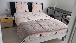 A neatly made bed with a quilted cover, a bedside lamp, a nightstand, and a small table with a lamp. - 2 BRIGHT ROOMS IN A HOMESTAY (Quincy-Voisins)