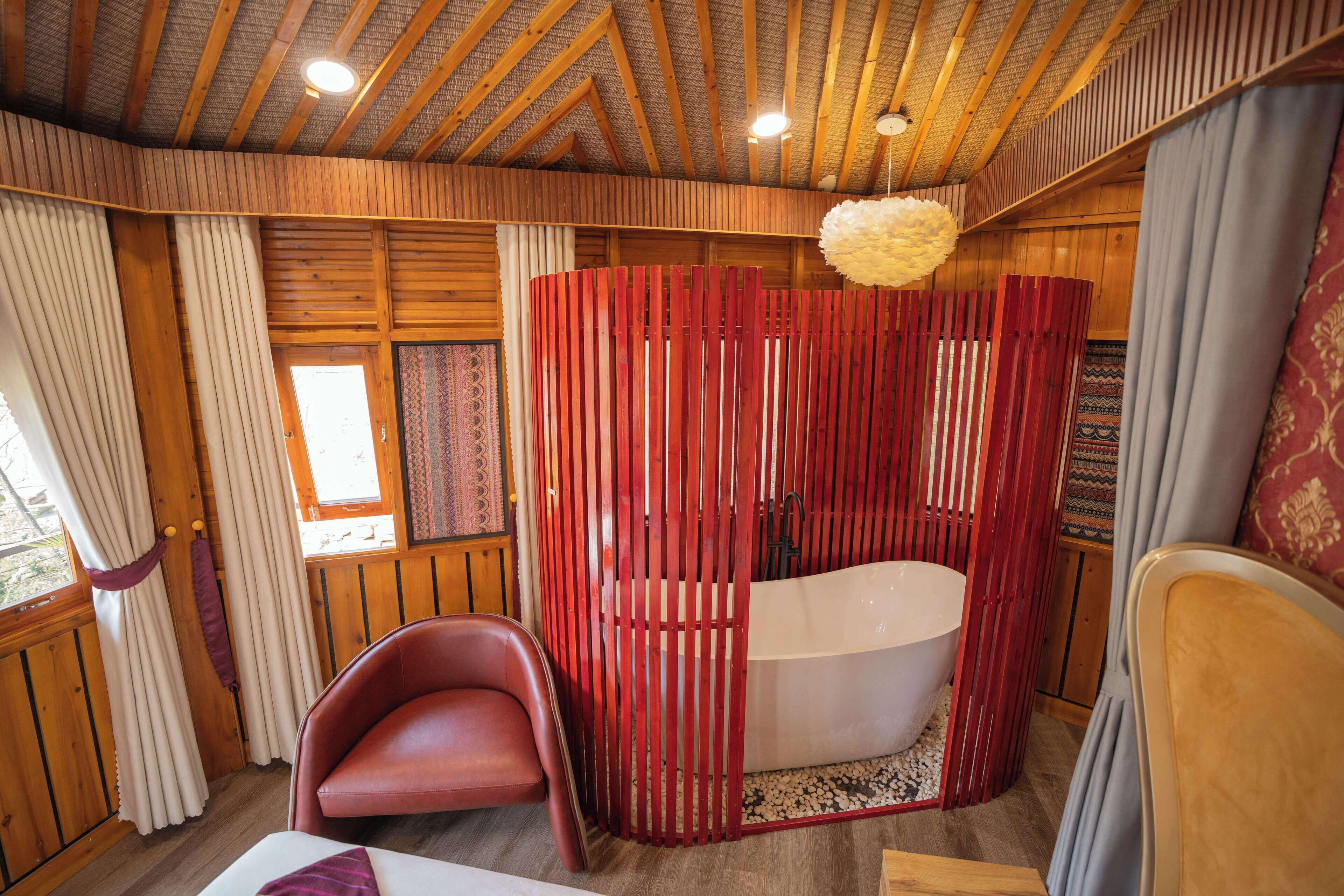 A wooden cabin interior with a bathtub, a red partition, and a chair.