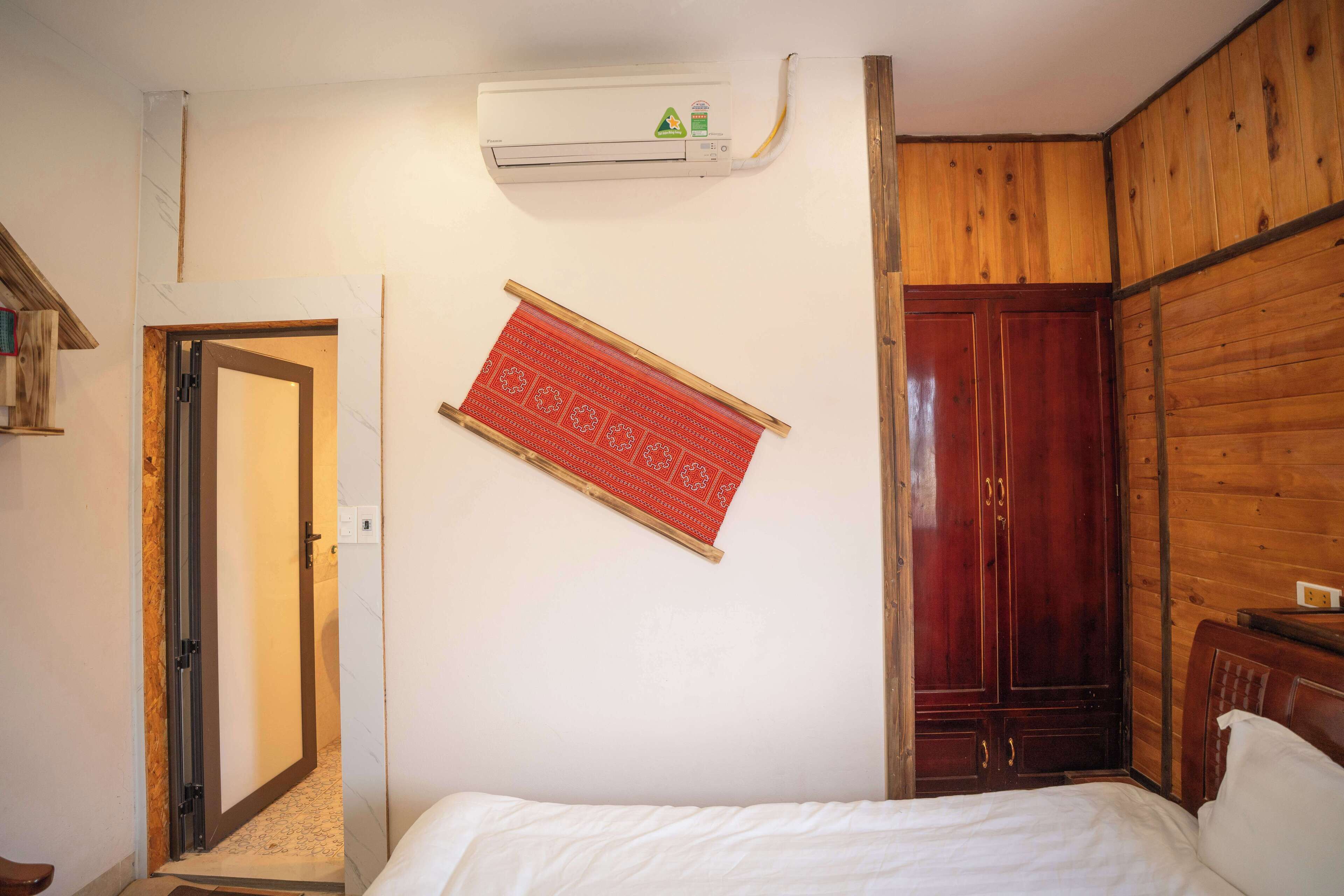 A bedroom with a bed, a wooden wardrobe, a red decorative panel, and an air conditioning unit.