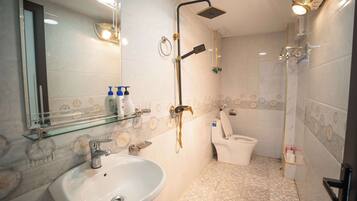 A bathroom with a sink, mirror, shower, toilet, and patterned tiles.