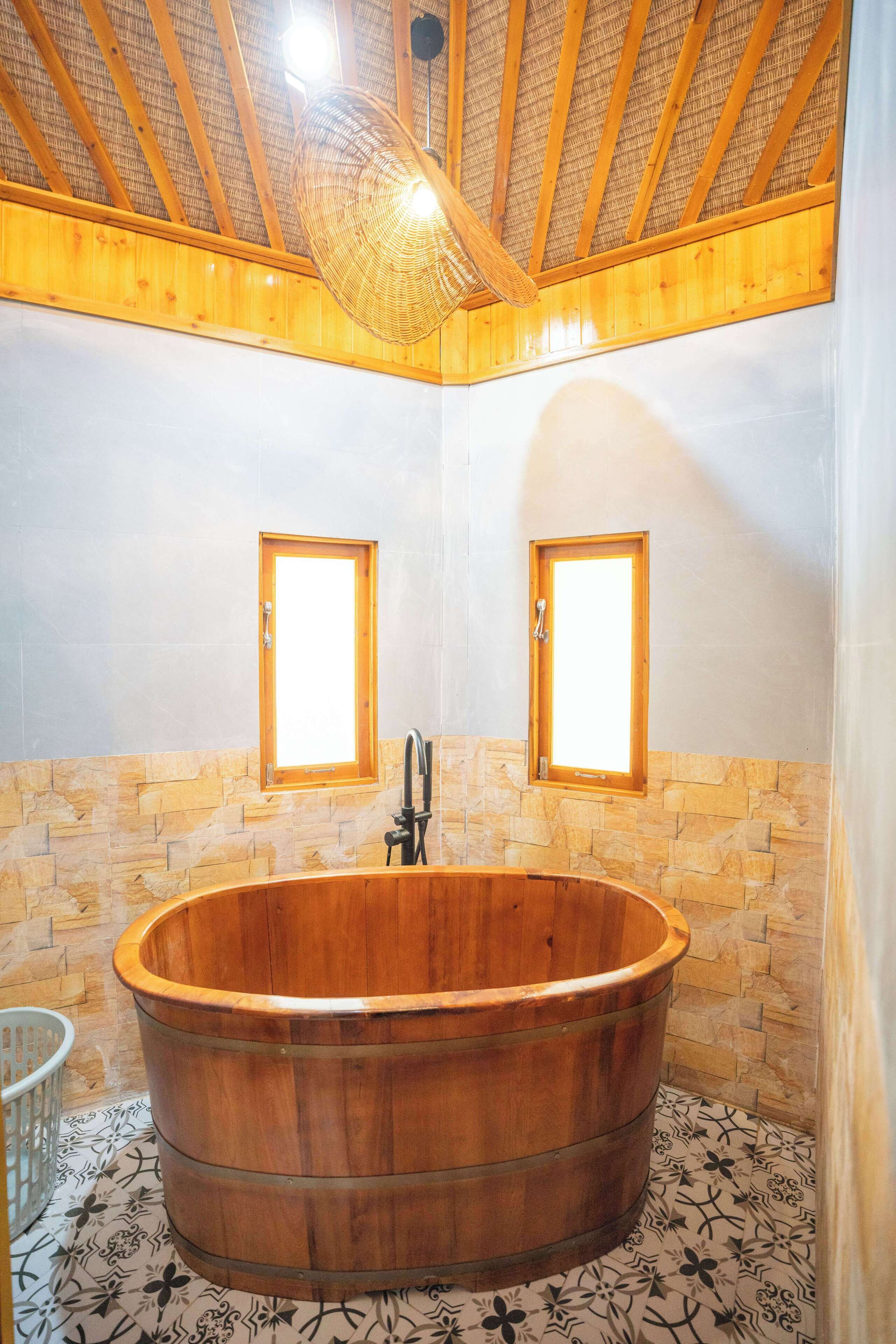 A wooden bathtub in a corner bathroom with stone walls and a sloped ceiling.