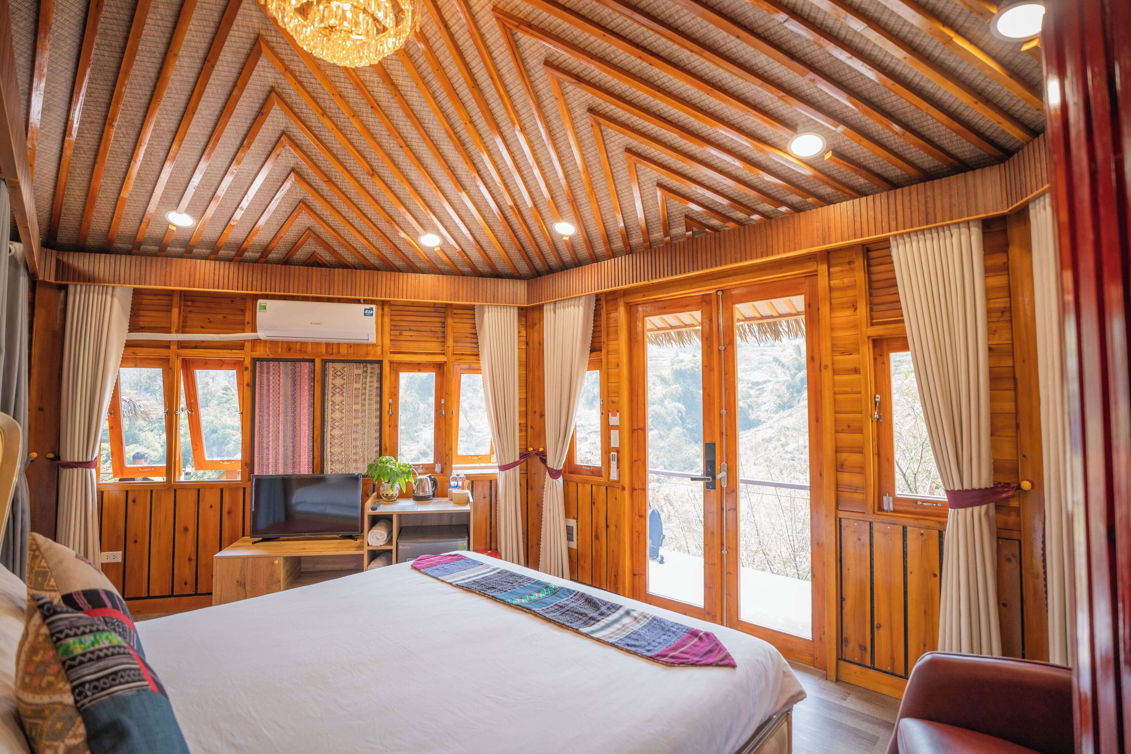 Un dormitorio de cabaña de madera con una cama, un escritorio con un ordenador y ventanas grandes.