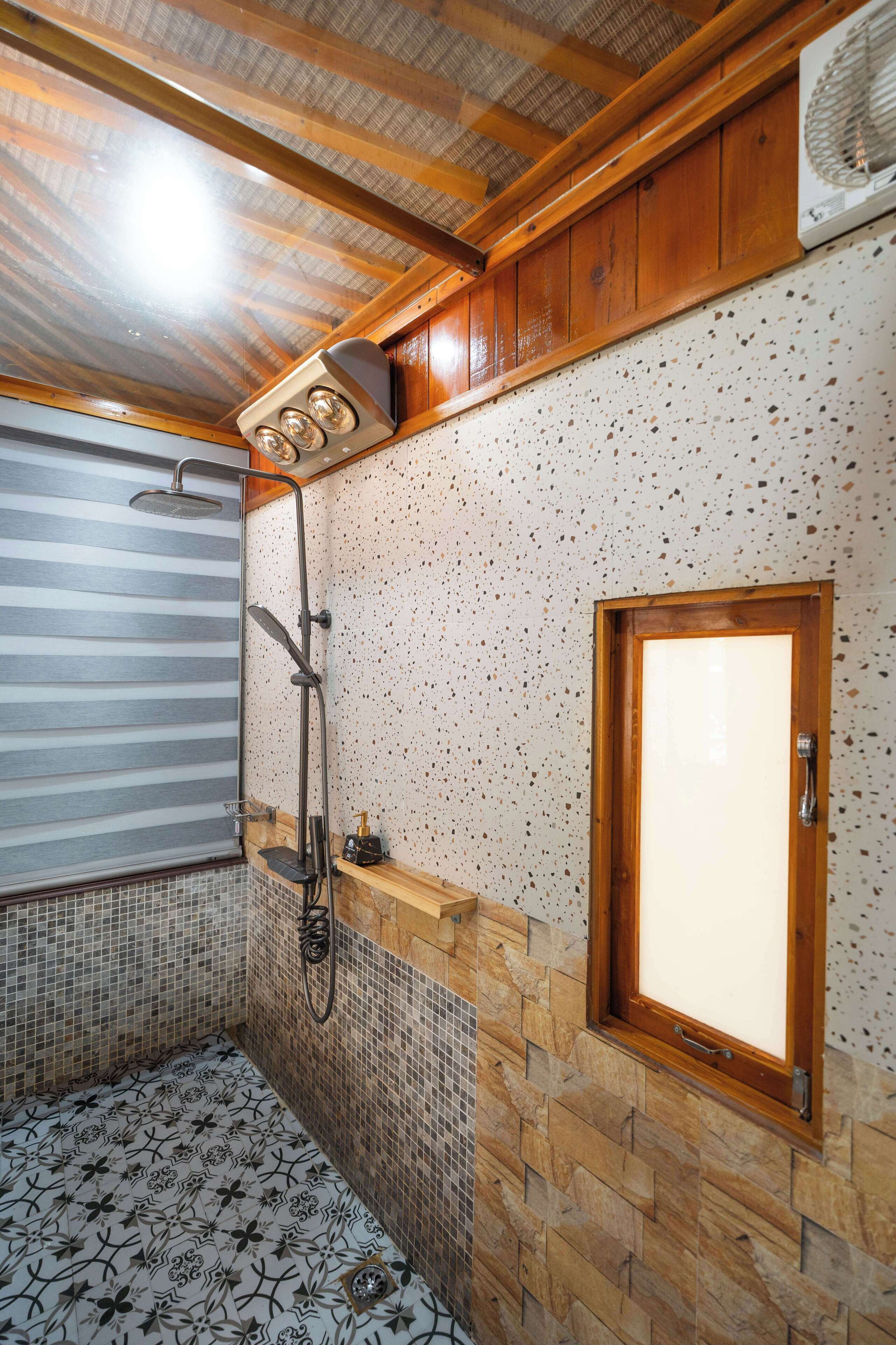Une salle de bain avec une douche, des murs carrelés, un meuble-lavabo en bois et une fenêtre.