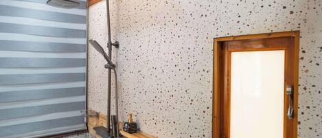 Une salle de bain avec une douche, des murs carrelés, un meuble-lavabo en bois et une fenêtre.