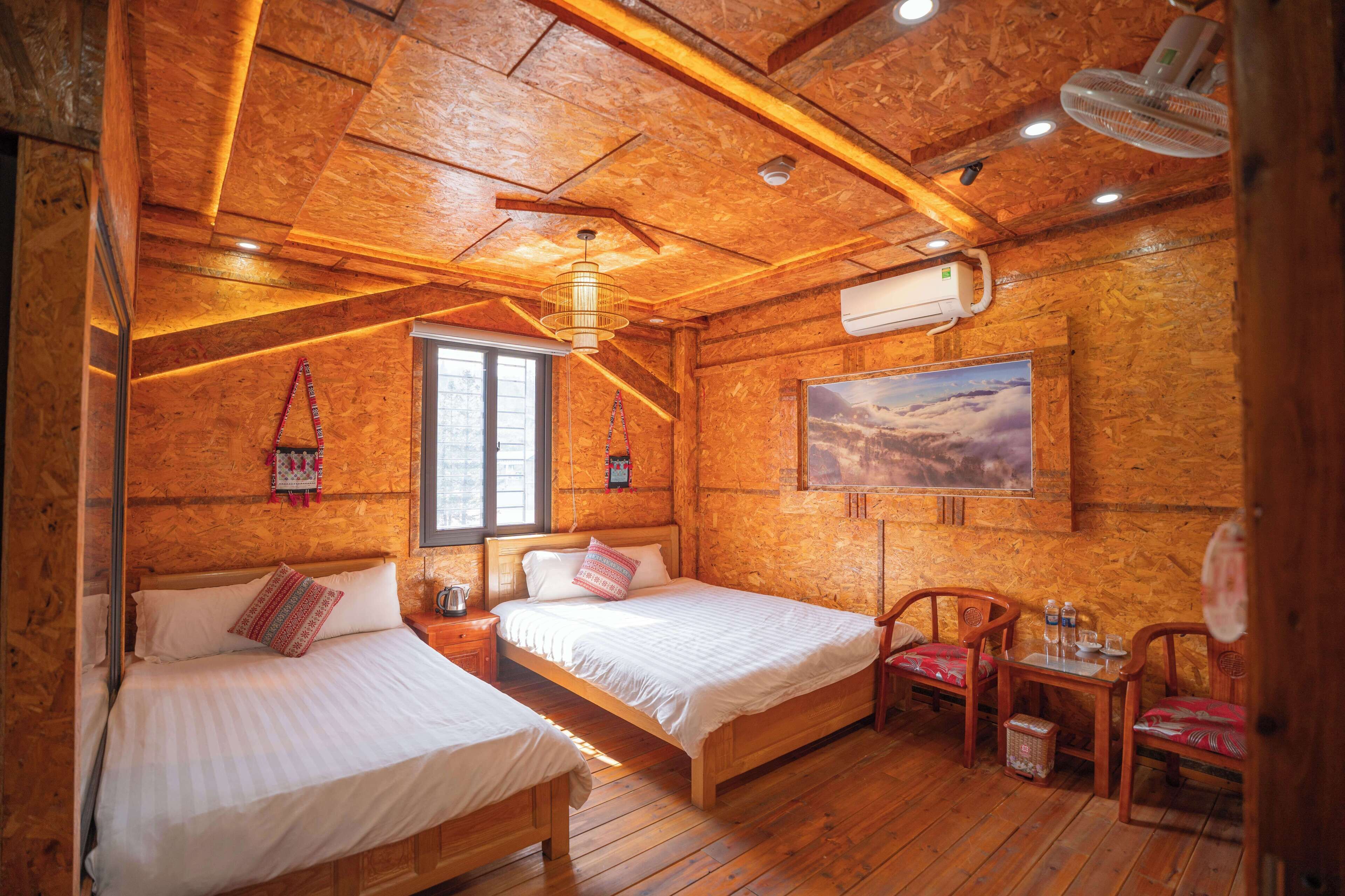 A wooden cabin with two beds, a dining table, chairs, a ceiling fan, and a mounted TV.