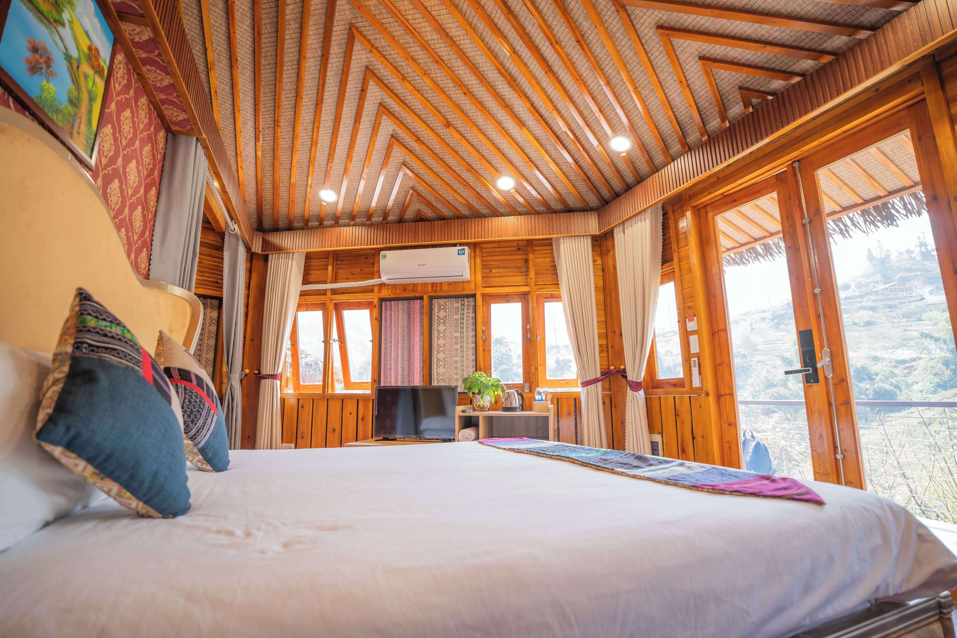 A spacious bedroom with a large bed, wooden ceiling, and large windows offering a view of the outdoors.