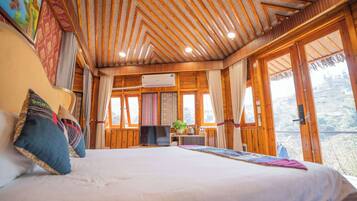 A spacious bedroom with a large bed, wooden ceiling, and large windows offering a view of the outdoors.