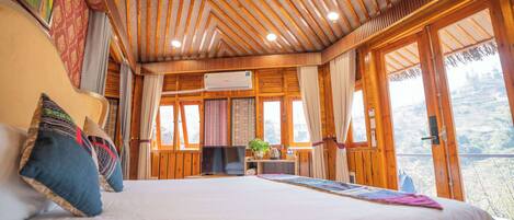Un dormitorio amplio con una cama grande, techo de madera y ventanas grandes que ofrecen vistas al exterior.