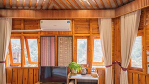 A wooden cabin room with a TV, a shelf with towels, a plant, and a window with curtains. - Sinai Bungalow & Hotel SaPa (Sa Pa)