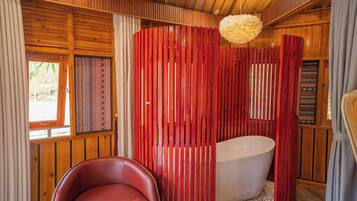 A wooden cabin interior with a red striped partition, a white bathtub, and a red leather chair.