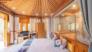 A spacious room with a large bed, wooden ceiling, and a glass shower area.