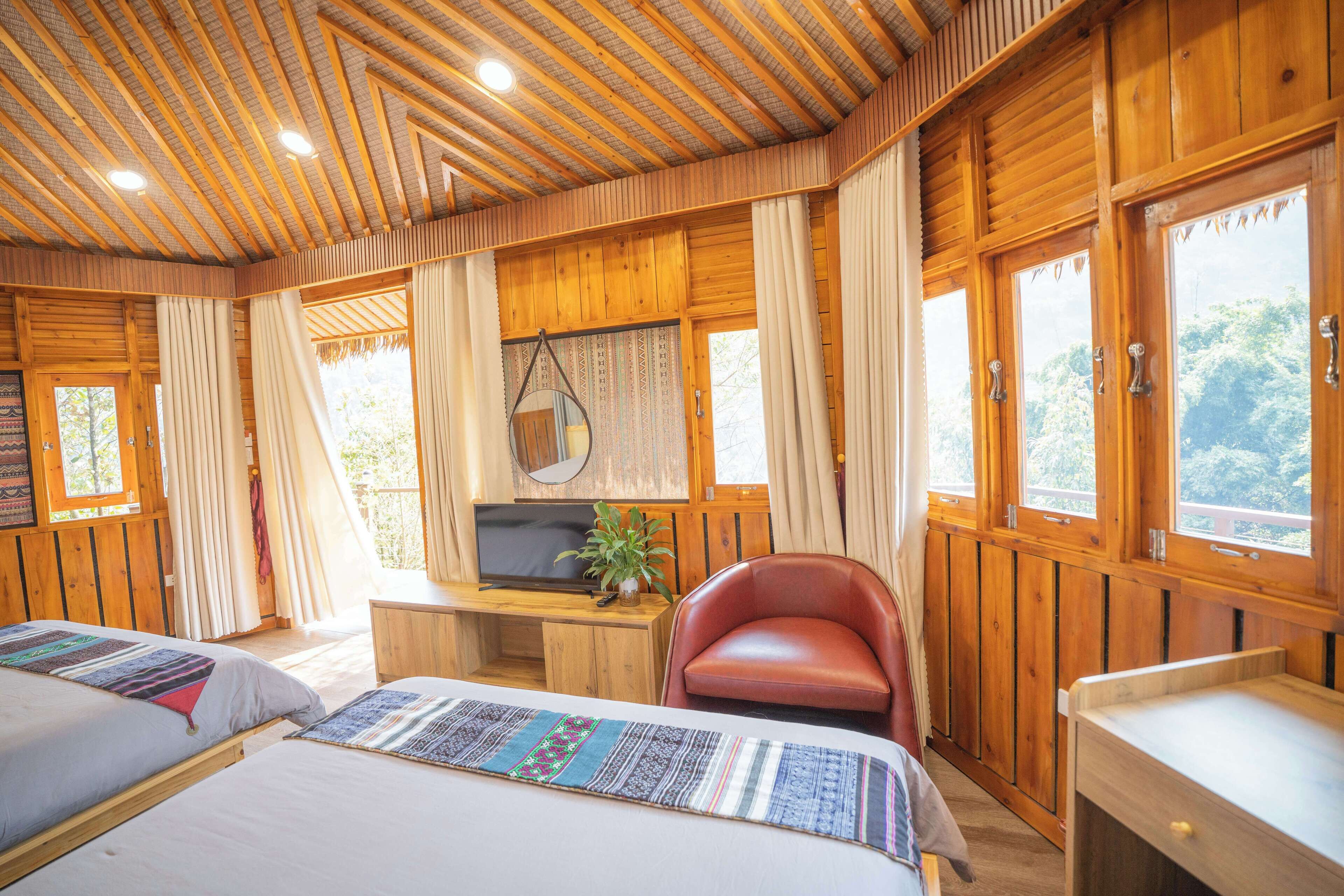 Una habitación tipo cabaña de madera con dos camas, un televisor, un escritorio y una silla roja.