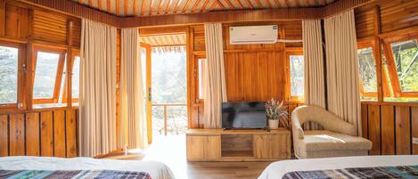 A wooden cabin room with two beds, a TV, and a sofa.