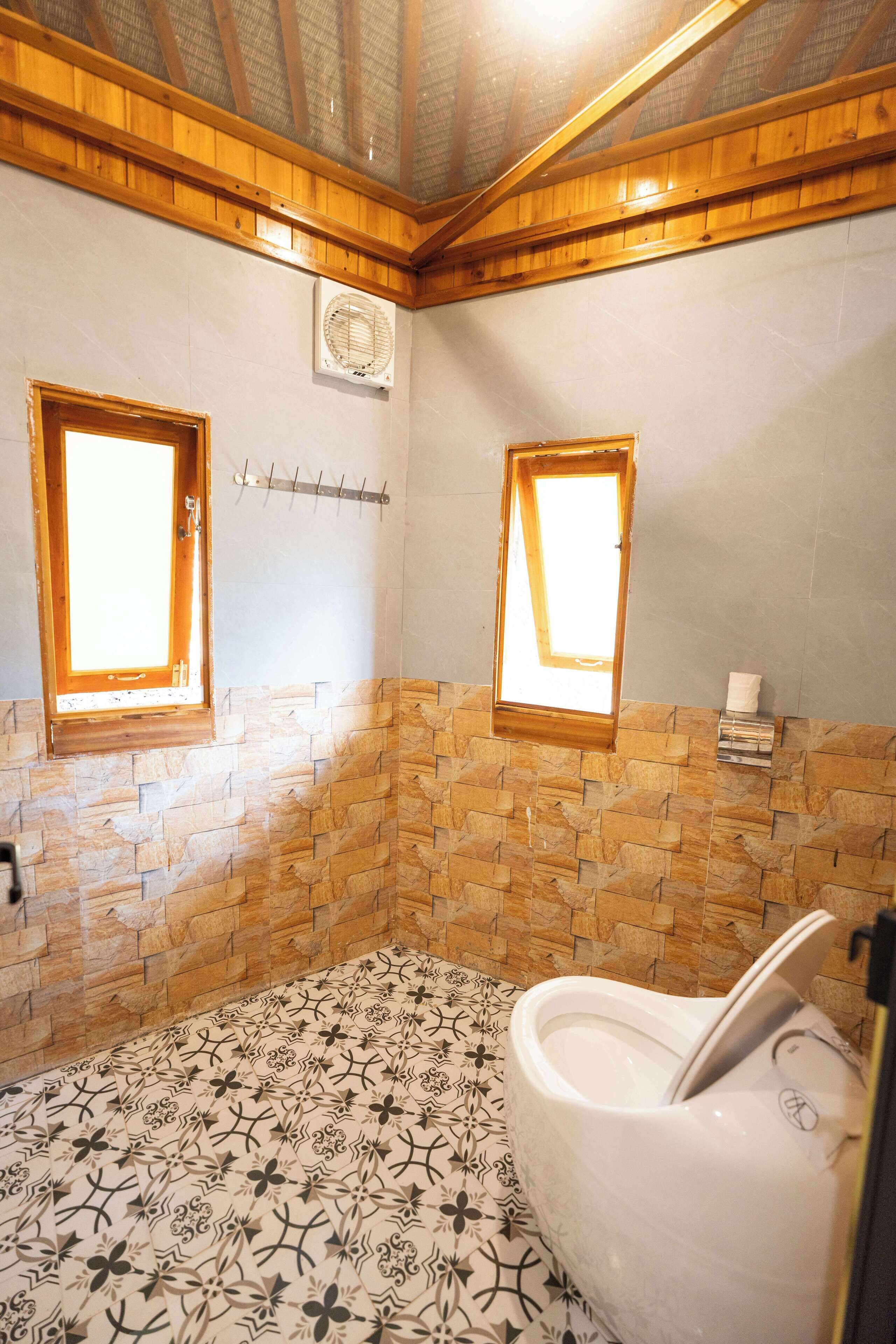 A bathroom with a stone-patterned floor, a bathtub, and two windows with wooden frames.