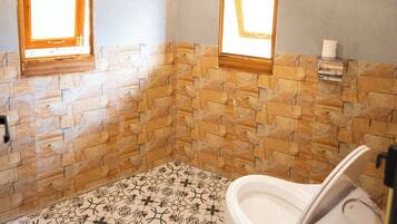 A bathroom with a stone-patterned floor, a bathtub, and two windows with wooden frames.
