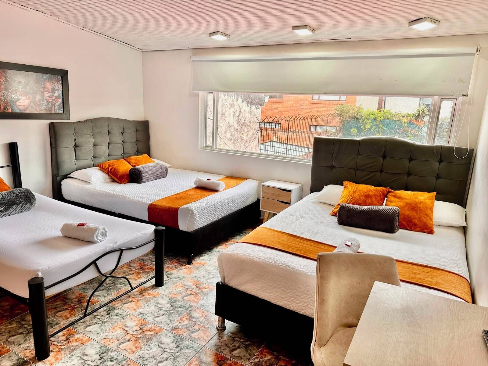 A hotel room with two beds, a small table, a chair, and a window with a view of the outside.