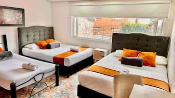 A hotel room with two beds, a small table, a chair, and a window with a view of the outside.
