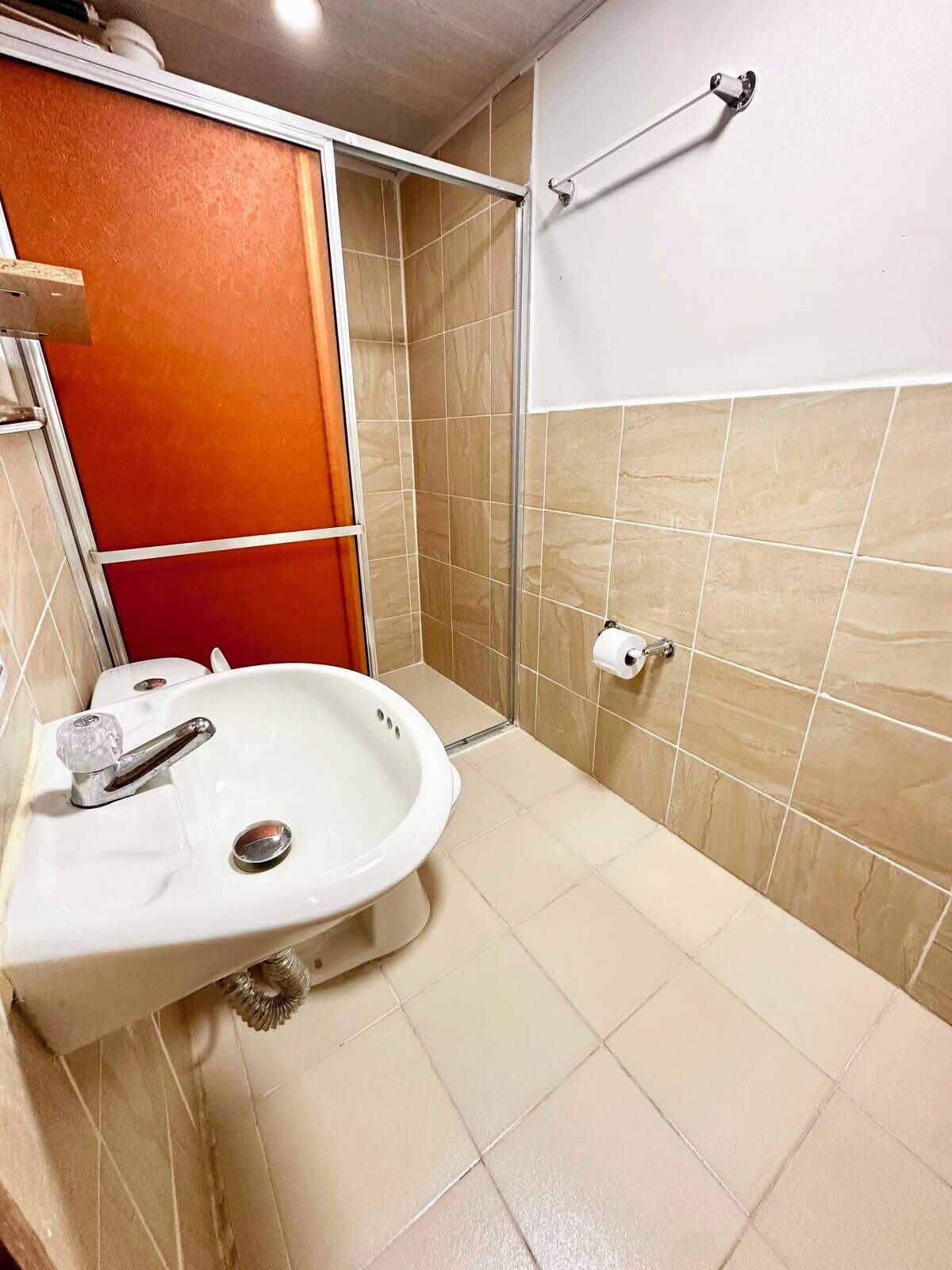 A bathroom with a white sink, a shower with a glass door, and beige tiled walls.