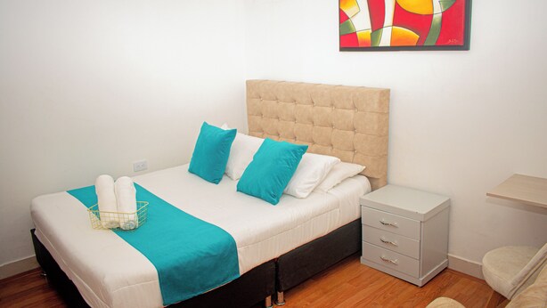 Una cama bien hecha con cabecera, una mesita de noche con cajones y una obra de arte colgada en la pared.