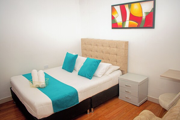 A neatly made bed with a headboard, a bedside table with drawers, and a wall-mounted artwork. - Hotel Flamante bulevar (Bogotá)