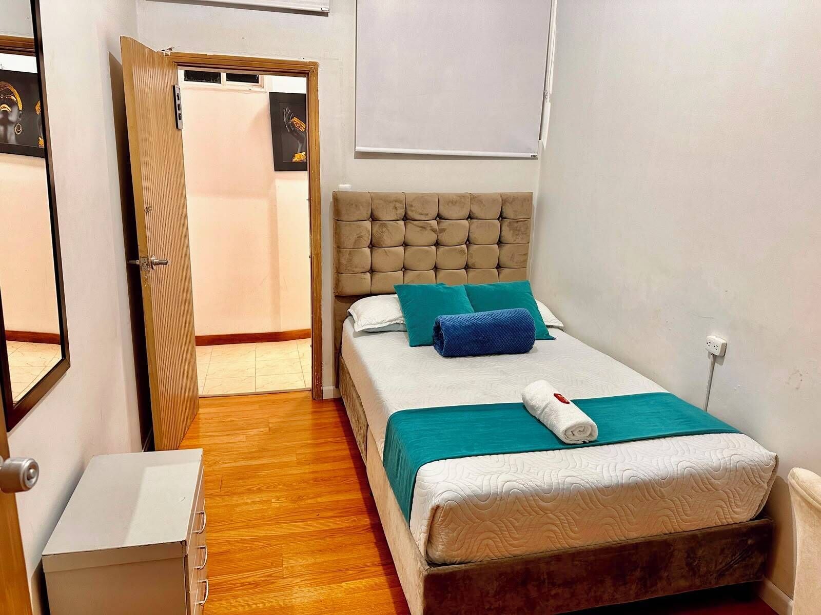 Un dormitorio con cama, mesita de noche, puerta y lámpara de pared.