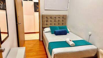 Un dormitorio con cama, mesita de noche, puerta y lámpara de pared.