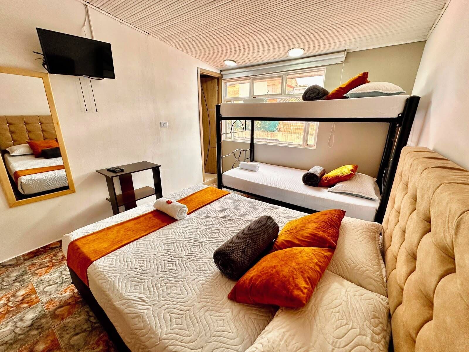 A hotel room with bunk beds, a television, a mirror, and a bed with patterned bedding.