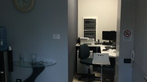 Un petit bureau avec un bureau, une chaise, un ordinateur et une horloge au mur.