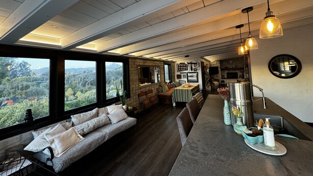Ein großzügiger Wohnbereich mit einem großen Fenster und Blick auf eine reizvolle Landschaft, eine gemütliche Sitzecke und eine Küche mit modernen Geräten.