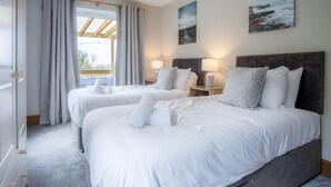 A hotel room with two beds, a large window with curtains, a wooden headboard, and two bedside lamps.