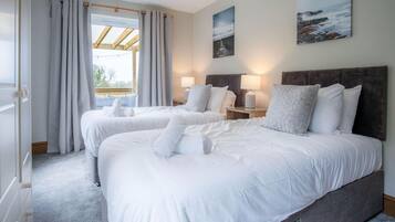 A hotel room with two beds, a large window with curtains, a wooden headboard, and two bedside lamps.