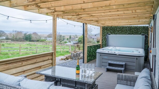 An outdoor patio with a hot tub, seating area, and a table with glasses and a bottle.