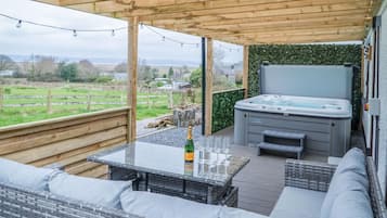 An outdoor patio with a hot tub, seating area, and a table with glasses and a bottle.