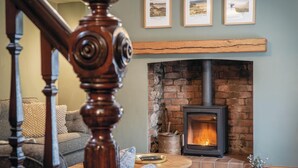 A cozy living room with a fireplace, a staircase, and three framed pictures on the wall.