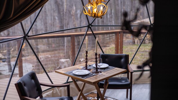 A dining area with a table set for two, candles, and a chandelier. - Domes at Catskills a lakefront glamping adventure for adults (Swan Lake)