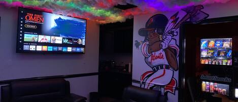 Une pièce dotée d’un grand téléviseur diffusant un film, d’une fresque représentant un joueur de baseball et d’un distributeur automatique.