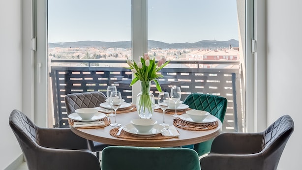 A dining table set with plates, bowls, and glasses, a vase with flowers, and two chairs.