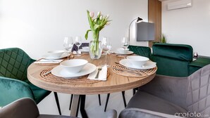 A dining table set for six with white bowls, plates, and cutlery, surrounded by green upholstered chairs.