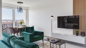 A modern living room with a green sofa, a dining table, and a TV mounted on the wall.