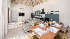 A modern living room with a dining area, a kitchen, and a TV mounted on the wall.